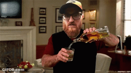 A Man Is Pouring Whiskey Into A Glass In A Living Room GIF