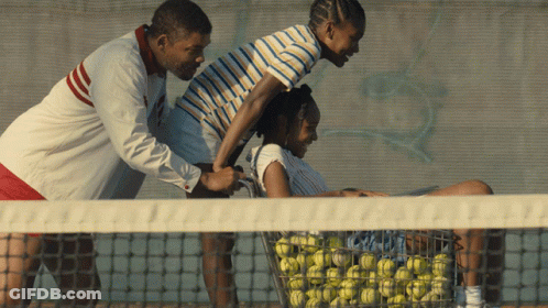 A Man Is Pushing A Woman On A Tennis Court With A Basket Full Of Tennis Balls GIF