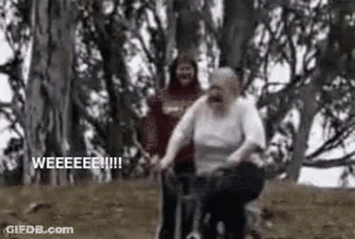 A Man Is Pushing An Elderly Woman On A Bicycle In A Forest . GIF