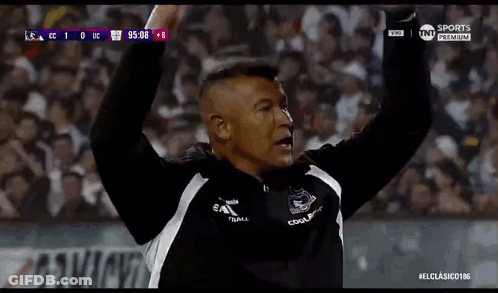 A Man Is Raising His Arms In The Air While Watching A Soccer Game . GIF