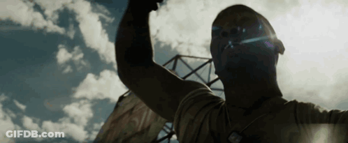 A Man Is Raising His Fist In The Air In Front Of A Blue Sky With Clouds . GIF