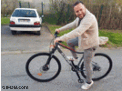 A Man Is Riding A Bicycle On A Street Next To A Car . GIF