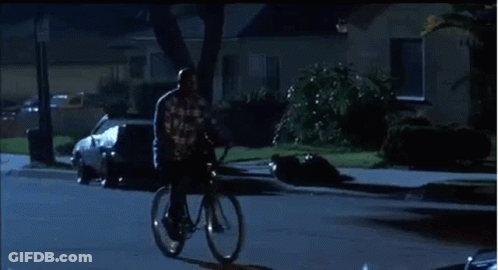 A Man Is Riding A Bike Down A City Street At Night . GIF