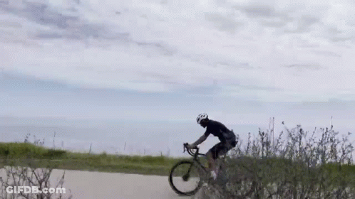 A Man Is Riding A Bike Down A Dirt Road Next To A Bush . GIF