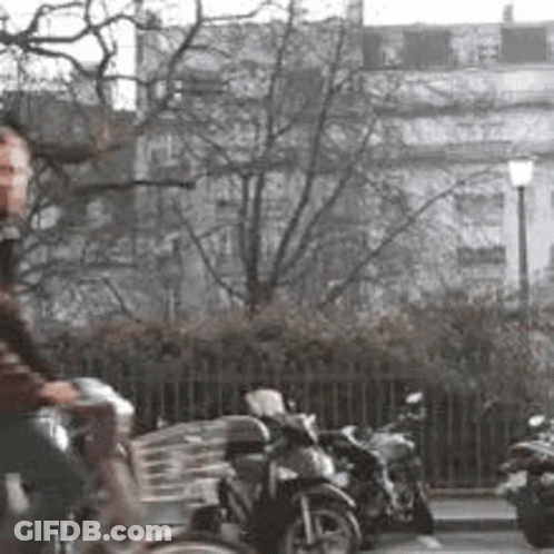A Man Is Riding A Bike Down A Street In Front Of A Row Of Parked Motorcycles . GIF