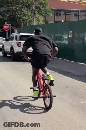 A Man Is Riding A Bike In Front Of A Red Stop Sign GIF