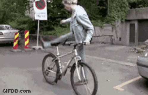 A Man Is Riding A Bike On A Street With A No Parking Sign Behind Him GIF