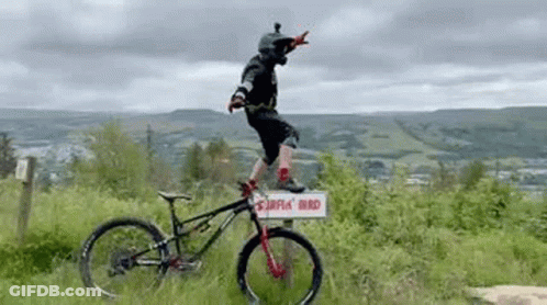 A Man Is Riding A Bike On Top Of A Sign In The Grass . GIF