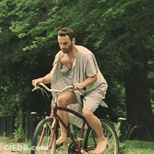 A Man Is Riding A Bike Without A Shirt On In A Park GIF