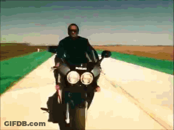A Man Is Riding A Black Suzuki Motorcycle Down A Road GIF
