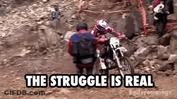 A Man Is Riding A Dirt Bike On A Rocky Trail While Another Man Sits On The Back Of It . GIF