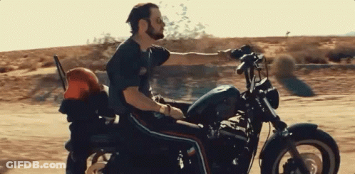 A Man Is Riding A Harley Davidson Motorcycle Down A Dirt Road GIF