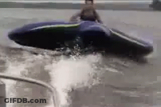 A Man Is Riding A Jet Ski Through A Flooded Area . GIF