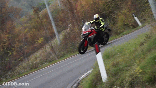 A Man Is Riding A Motorcycle Down A Road With A Red And Black Stripe On The Side GIF