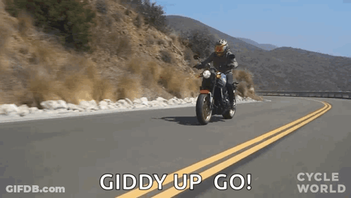 A Man Is Riding A Motorcycle Down A Road With The Words Giddy Up Go Behind Him . GIF