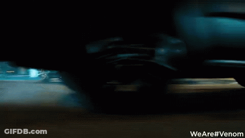 A Man Is Riding A Motorcycle Down A Street With A Sign That Says We Are #Venom GIF