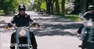 A Man Is Riding A Motorcycle Down A Street With Trees In The Background . GIF