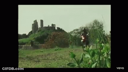 A Man Is Riding A Motorcycle In A Field In Front Of A Castle . GIF