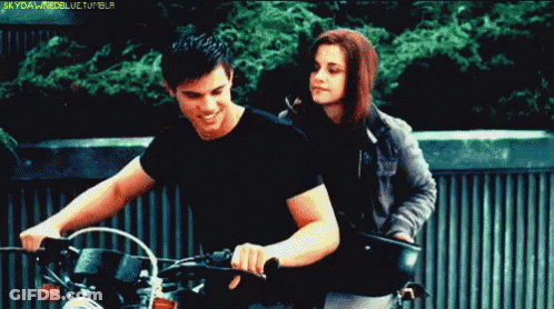 A Man Is Riding A Motorcycle Next To A Woman Who Is Standing Behind Him And The Words Skyfallmodellife Tumblr Are Visibl GIF