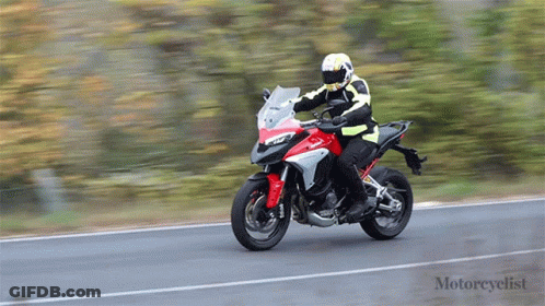 A Man Is Riding A Red And White Motorcycle On A Road GIF