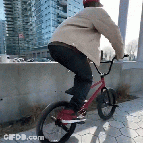 A Man Is Riding A Red Bike On A Sidewalk GIF