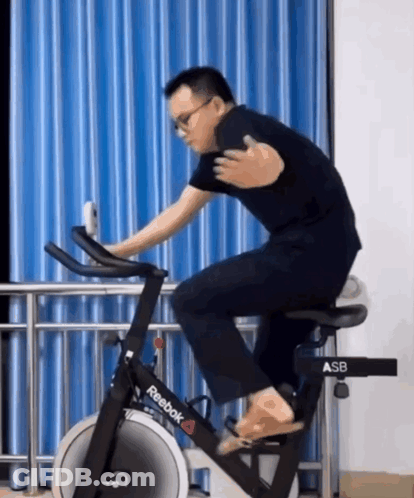 A Man Is Riding A Reebok Exercise Bike In Front Of A Blue Curtain GIF