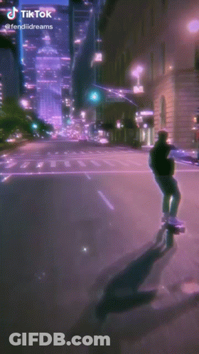 A Man Is Riding A Skateboard Down A Street At Night . GIF
