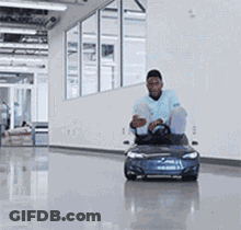 A Man Is Riding A Small Blue Car In A Hallway . GIF