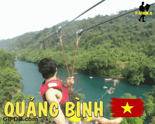 A Man Is Riding A Zip Line Over A River With Quang Binh In Yellow Letters GIF