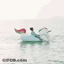 A Man Is Riding An Inflatable Unicorn In The Water . GIF