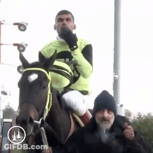 A Man Is Riding On The Back Of A Horse While Another Man Stands Behind Him . GIF