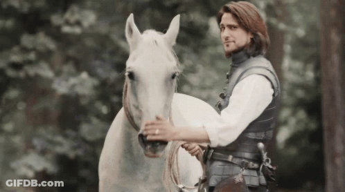 A Man Is Riding On The Back Of A White Horse In The Woods . GIF