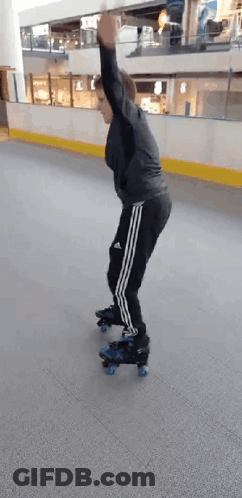 A Man Is Rollerblading On An Indoor Rink With His Arms In The Air . GIF