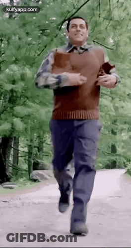 A Man Is Running Down A Dirt Road In The Woods . GIF