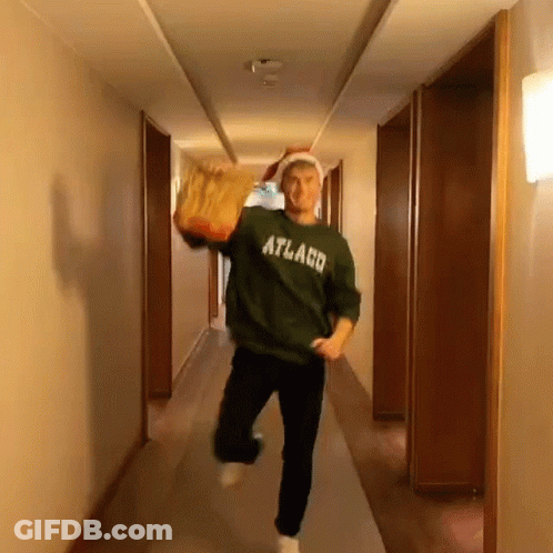 A Man Is Running Down A Hallway Wearing A Green Sweater That Says Atlaco GIF