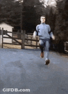 A Man Is Running Down A Road In Front Of A Fence GIF