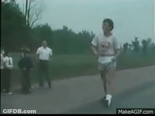 A Man Is Running Down A Road With A Group Of People Watching . GIF