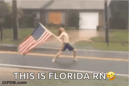 A Man Is Running Down A Street Holding An American Flag . GIF