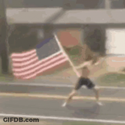 A Man Is Running Down A Street While Holding An American Flag . GIF