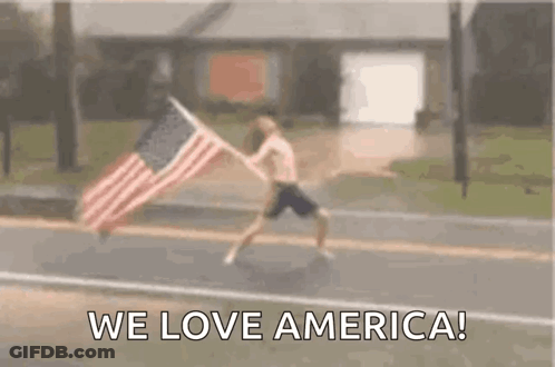 A Man Is Running Down A Street With An American Flag . GIF