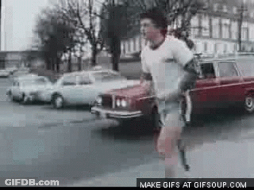 A Man Is Running Down The Street In Front Of A Car . GIF