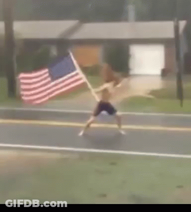 A Man Is Running Down The Street With An American Flag GIF