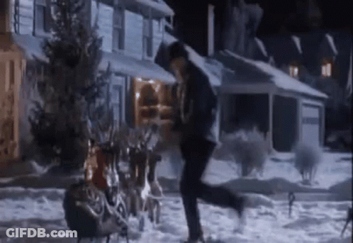 A Man Is Running In The Snow In Front Of A House With A Sleigh Full Of Reindeer . GIF