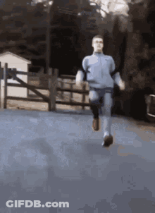 A Man Is Running On A Road With A Fence In The Background . GIF