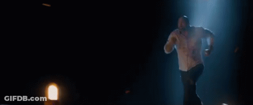 A Man Is Running Through A Dark Room With A Blue Light Coming From Behind Him . GIF