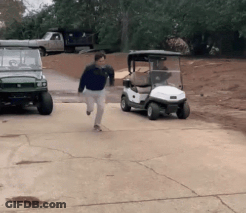 A Man Is Running Towards A Golf Cart That Is Parked In A Driveway GIF