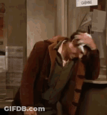 A Man Is Scratching His Head While Sitting At A Counter In A Store . GIF