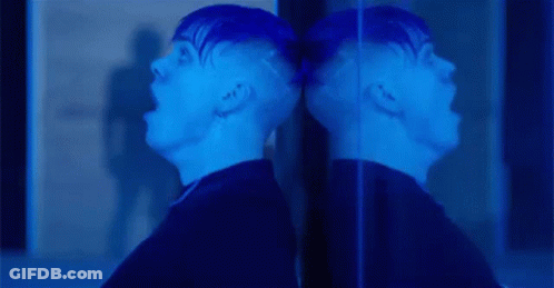A Man Is Screaming In Front Of A Mirror And His Reflection Is Visible . GIF
