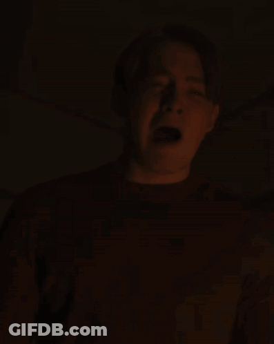 A Man Is Screaming In The Dark With His Mouth Open And His Tongue Sticking Out GIF