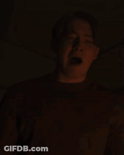 A Man Is Screaming In The Dark With His Mouth Open And His Tongue Sticking Out GIF